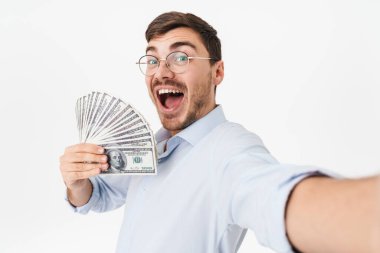 Gözlüklü, elinde dolar olan ve beyaz arka planda izole edilmiş selfie çeken mutlu bir adamın fotoğrafı.