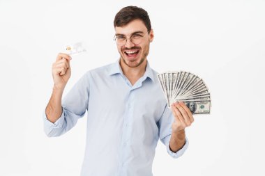 Gözlüklü, elinde dolar ve kredi kartı olan mutlu bir adamın fotoğrafı beyaz arka planda izole edilmiş.