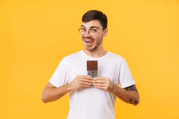 Фото Молодого Человека Очках Держащего Шоколад Облизывающего Губы Желтом Фоне — стоковое фото