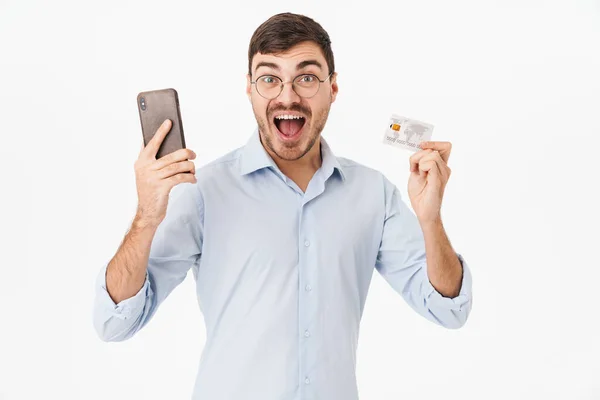 白い背景の上に隔離された携帯電話やクレジットカードを保持眼鏡で喜びの男の写真 — ストック写真