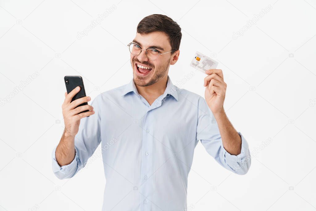 Photo of delighted man in eyeglasses holding cellphone and credit card isolated over white background
