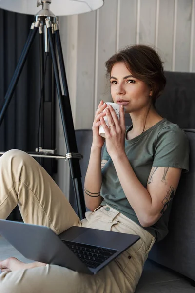 Atrakcyjna Młoda Kobieta Siedząca Kanapie Salonie Korzystająca Laptopa Pijąca Kawę — Zdjęcie stockowe