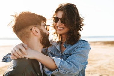 Genç ve güzel bir çift güneşli sahilde harika vakit geçiriyorlar, sarılıyorlar.