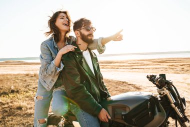 Güneşli sahilde motosiklet üzerinde oturan ceketli güzel Yong çifti.