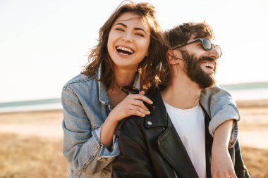 Mutlu genç çift güneşli sahilde birlikte eğleniyor, sarılıyorlar.