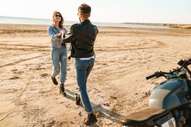 Güzel genç çift güneşli sahilde harika vakit geçiriyorlar, yürüyorlar.