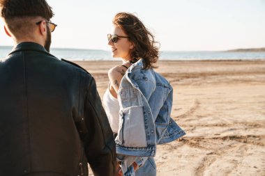 Güzel genç çift güneşli sahilde harika vakit geçiriyorlar, yürüyorlar.