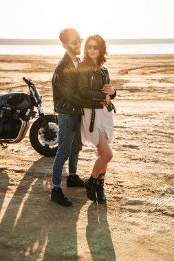 Ceket giyen genç ve güzel Cople güneşli sahilde vakit geçiriyor, motosikletin yanında duruyor, sarılıyor.
