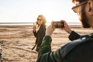 Genç ve güzel bir çift güneşli plajda harika vakit geçiriyorlar. Erkek, kız arkadaşının fotoğrafını çekiyor.