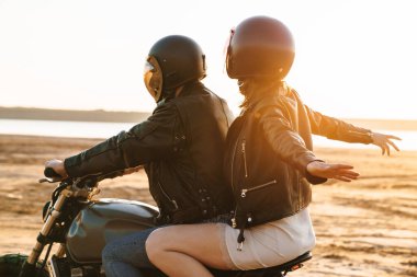 Güzel, genç, şık bir çift plajda motosiklet sürerken eğleniyor.