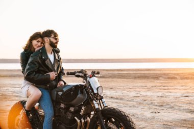Güzel, genç, şık bir çift plajda motosiklet sürerken eğleniyor.