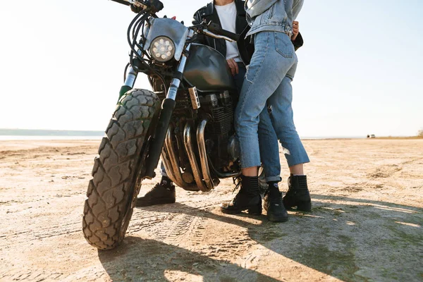 日当たりの良いビーチでバイクにもたれながら抱き合っている若いカップルの作物のイメージ — ストック写真