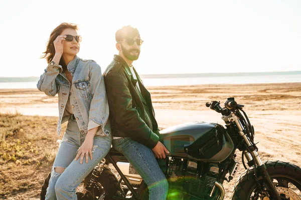 在阳光明媚的海滩边骑摩托车时迷人的年轻夫妇拥抱在一起 — 图库照片