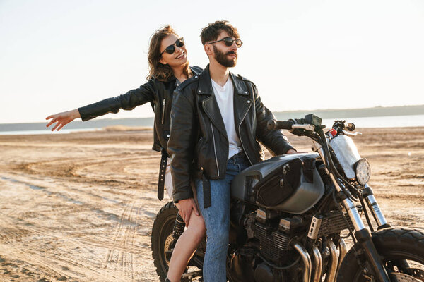 Beatiful yong couple wearing jackets sitting on a motorbike at the sunny beach