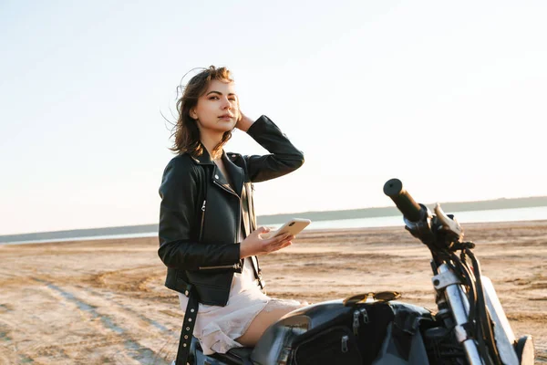 Красивая Молодая Девушка Кожаной Куртке Сидит Мотоцикле Солнечном Пляже Используя — стоковое фото