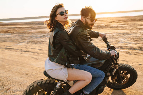 Beautiful young stylish couple enjoying ride on a motorbike at the beach