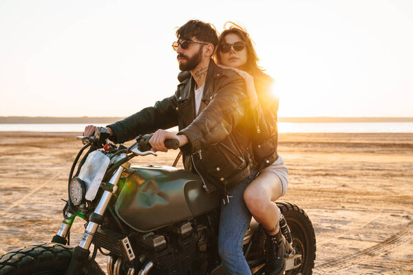 Beautiful young stylish couple enjoying ride on a motorbike at the beach