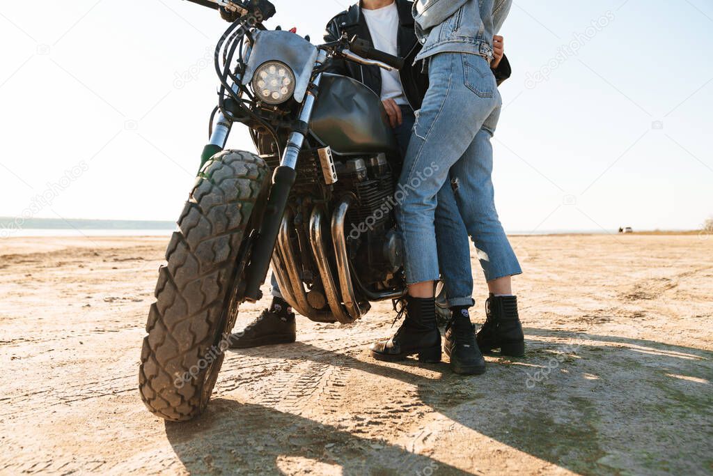 Cropped image of a young couple embracing while leaning on a motorbike at the sunny beach