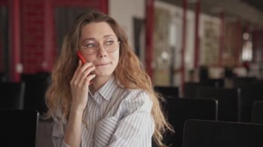 Genç ve mutlu bir kadın konferans salonunda otururken telefonla konuşuyor.