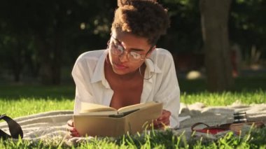 Çekici, Afro-Amerikan bir kadın parkta piknik sırasında kitap okuyor.