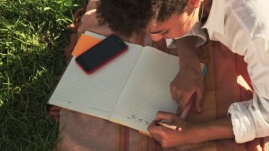 Genç bir Afro-Amerikalı kadının en iyi görüntüsü planlama kitabında çimlerin üzerinde yatıyor.