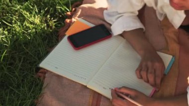 Genç bir Afro-Amerikalı kadının en iyi görüntüsü planlama kitabında çimlerin üzerinde oturuyor.