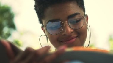Kulaklıklı, mutlu, Afro-Amerikan bir kadının yakın plan görüntüsü parkta oturan defterinde yazıyor.