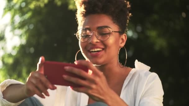 Щаслива Молода Афроамериканка Окулярами Дивиться Щось Смішне Своєму Смартфоні Тримаючи — стокове відео