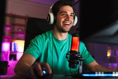 Kafkasyalı, kulaklıklı, bilgisayar başında kapalı bir masada otururken video oyunu oynayan adamın görüntüsü