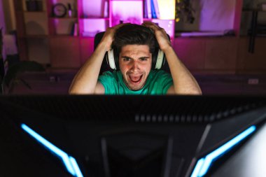 Kulaklıklı mutsuz bir gencin evde bilgisayar oyunu oynarken kafasını tutuşu.