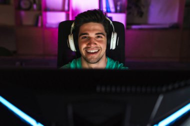 Kafkasyalı, kulaklıklı, bilgisayar başında kapalı bir masada otururken video oyunu oynayan adamın görüntüsü