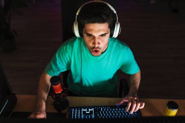 Kulaklıklı, bilgisayar başında evde otururken bilgisayar oyunu oynayan mutlu bir adamın görüntüsü