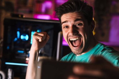 Memnuniyet verici bir jest yapan ve evde video oyunu oynarken cep telefonuyla selfie çeken adamın görüntüsü