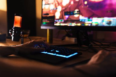 Kafkasyalı bir adamın kapalı bir masada otururken mikrofonla bilgisayar oyunu oynarken çekilmiş görüntüsü.