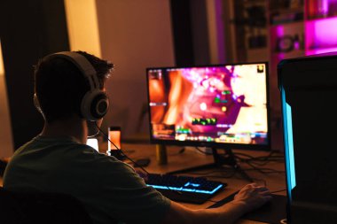 Kulaklıklı bir adamın masada otururken bilgisayar başında oyun oynaması görüntüsü