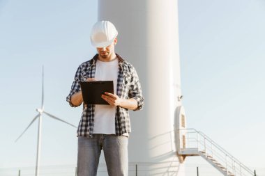 Yel değirmenleriyle dolu bir alanda durup not alan bir elektrik mühendisi.