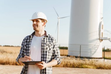 Yel değirmenleriyle dolu bir alanda durup not alan bir elektrik mühendisi.