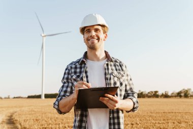 Yel değirmenleriyle dolu bir alanda durup not alan bir elektrik mühendisi.