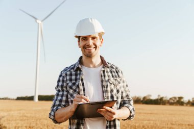 Yel değirmenleriyle dolu bir alanda durup not alan bir elektrik mühendisi.