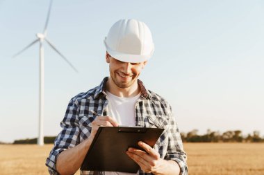 Yel değirmenleriyle dolu bir alanda durup not alan bir elektrik mühendisi.