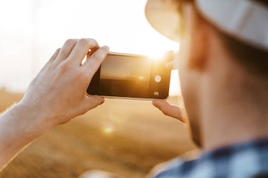 Bir tarlada rüzgar türbinlerinin fotoğrafını çeken kasklı bir işçi.