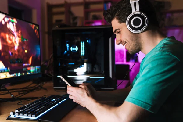 Imagem Jovem Alegre Fones Ouvido Usando Celular Enquanto Joga Videogame — Fotografia de Stock