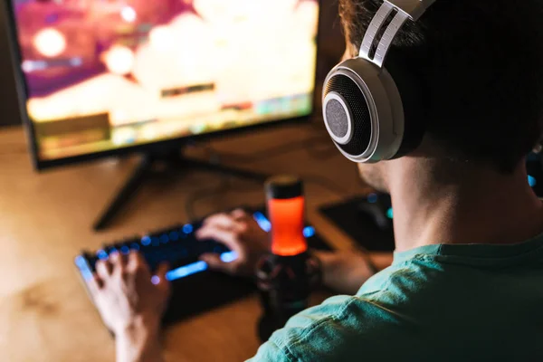 屋内のテーブルに座っている間 コンピュータ上でビデオゲームをプレイヘッドフォンで焦点を当てた男のイメージ — ストック写真