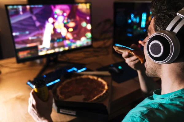 Bild Fokuserad Ung Man Hörlurar Äta Pizza Medan Spelar Spel — Stockfoto