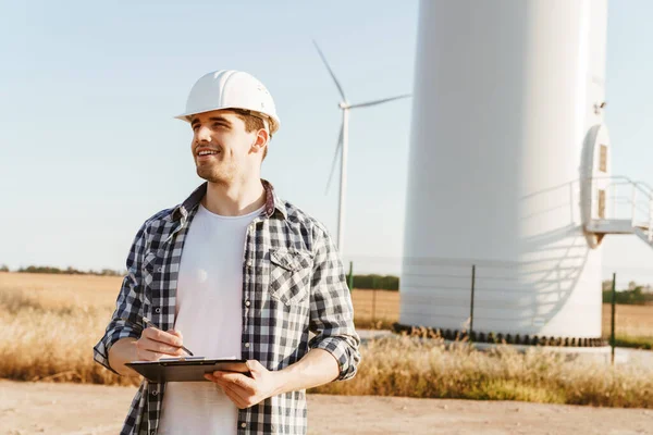 Yel değirmenleriyle dolu bir alanda durup not alan bir elektrik mühendisi.