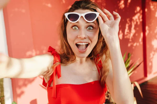 Bikinili ve güneş gözlüklü mutlu bir kadın dışarıda akıllı telefondan selfie çekiyor.