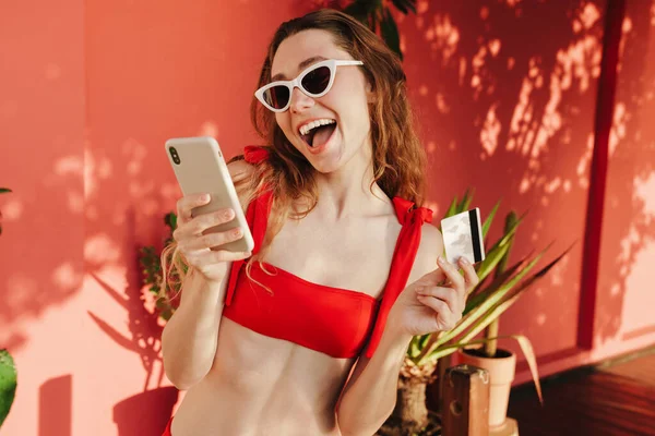 Dışarıda kredi kartı ve cep telefonuyla poz veren güzel genç bir kadın.