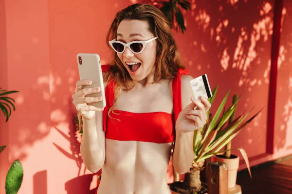 Dışarıda kredi kartı ve cep telefonuyla poz veren güzel genç bir kadın.