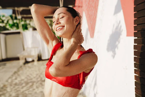 Bikinili çekici genç bir kadın sahilde duş alıyor.