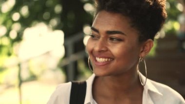 Mutlu, gülümseyen, Afro-Amerikan bir kadının yakından görüntüsü parkta yürüyor.